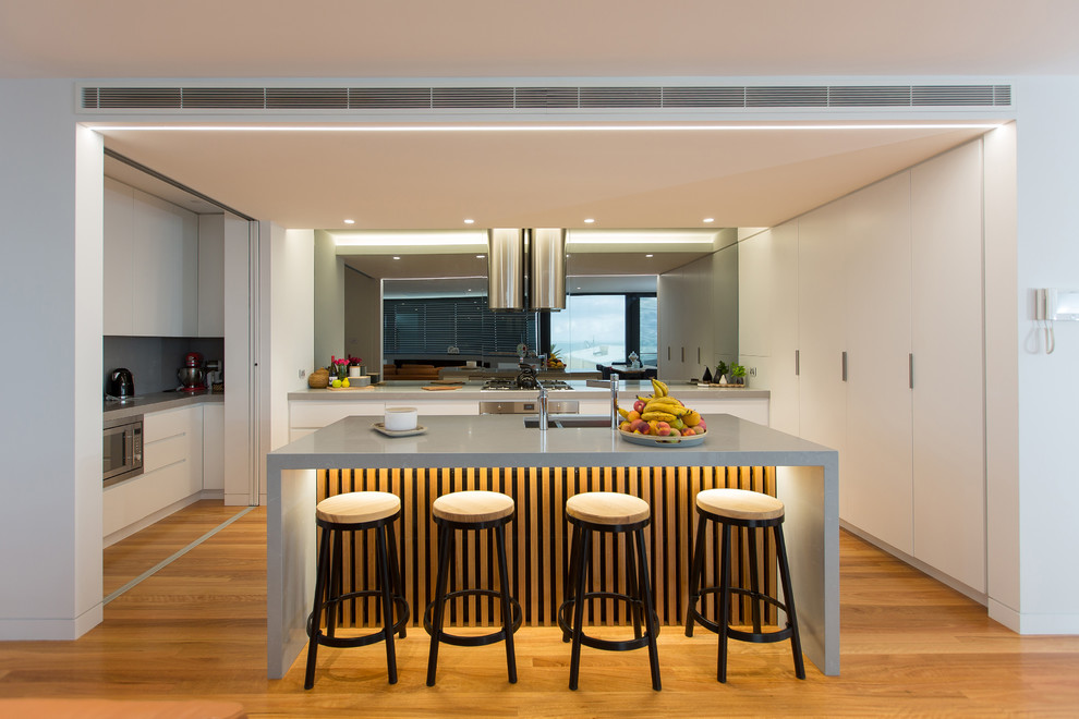 Inspiration for a large contemporary u-shaped separate kitchen in Newcastle - Maitland with light hardwood floors, a double-bowl sink, flat-panel cabinets, white cabinets, metallic splashback, mirror splashback, stainless steel appliances, with island and beige floor.