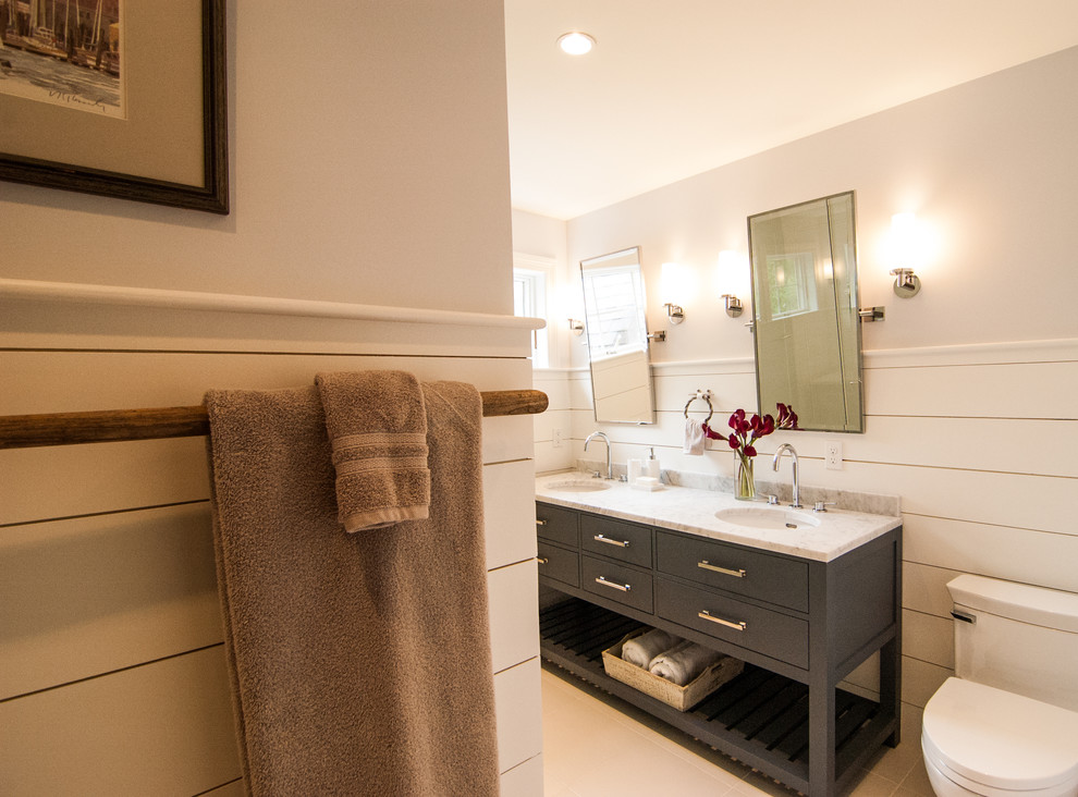Photo of a mid-sized beach style 3/4 bathroom in Portland Maine with flat-panel cabinets, dark wood cabinets, a corner shower, a one-piece toilet, beige tile, ceramic tile, beige walls, ceramic floors, a drop-in sink, marble benchtops and grey floor.