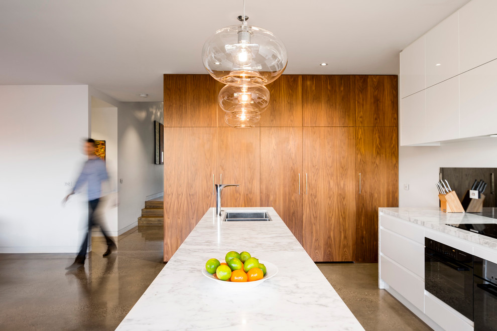 Mid-sized modern single-wall open plan kitchen in Melbourne with an undermount sink, flat-panel cabinets, light wood cabinets, marble benchtops, metallic splashback, glass sheet splashback, stainless steel appliances, concrete floors and with island.