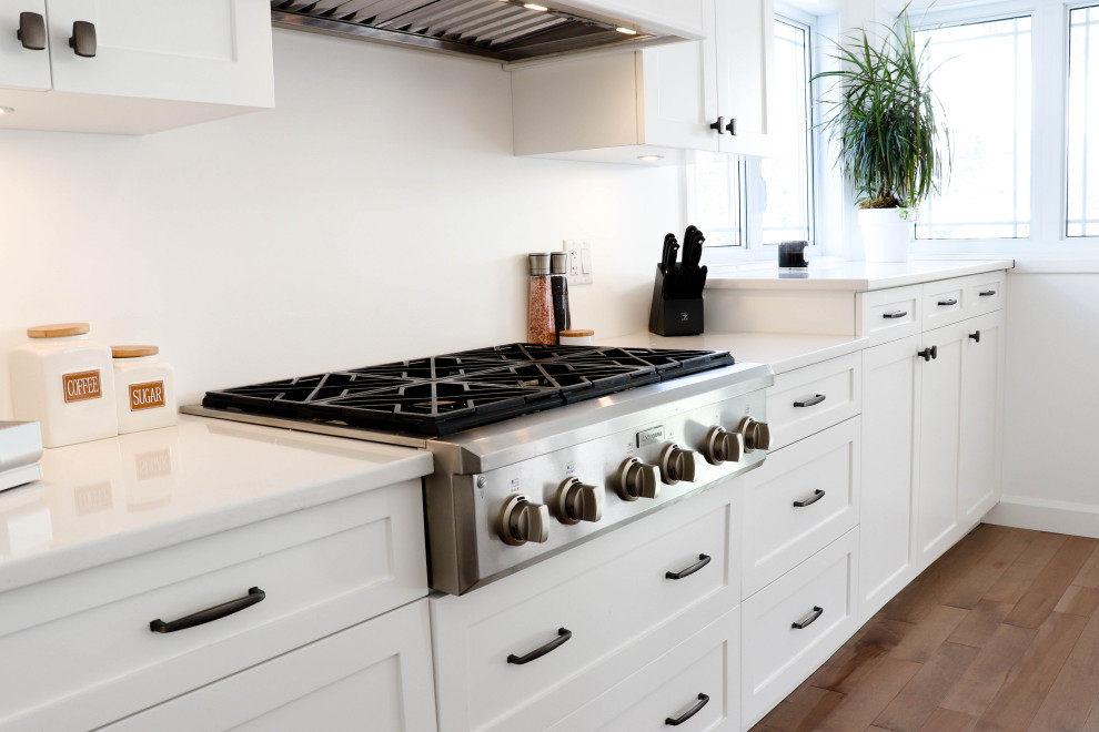 Inspiration for a large transitional l-shaped medium tone wood floor and brown floor open concept kitchen remodel with an undermount sink, shaker cabinets, white cabinets, quartzite countertops, white backsplash, ceramic backsplash, stainless steel appliances and an island