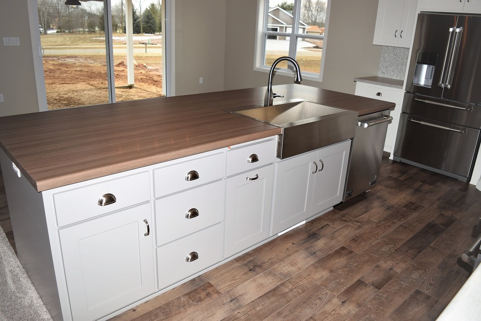 Large medium tone wood floor open concept kitchen photo with a drop-in sink, recessed-panel cabinets, white cabinets, laminate countertops, multicolored backsplash, ceramic backsplash, stainless steel appliances and an island