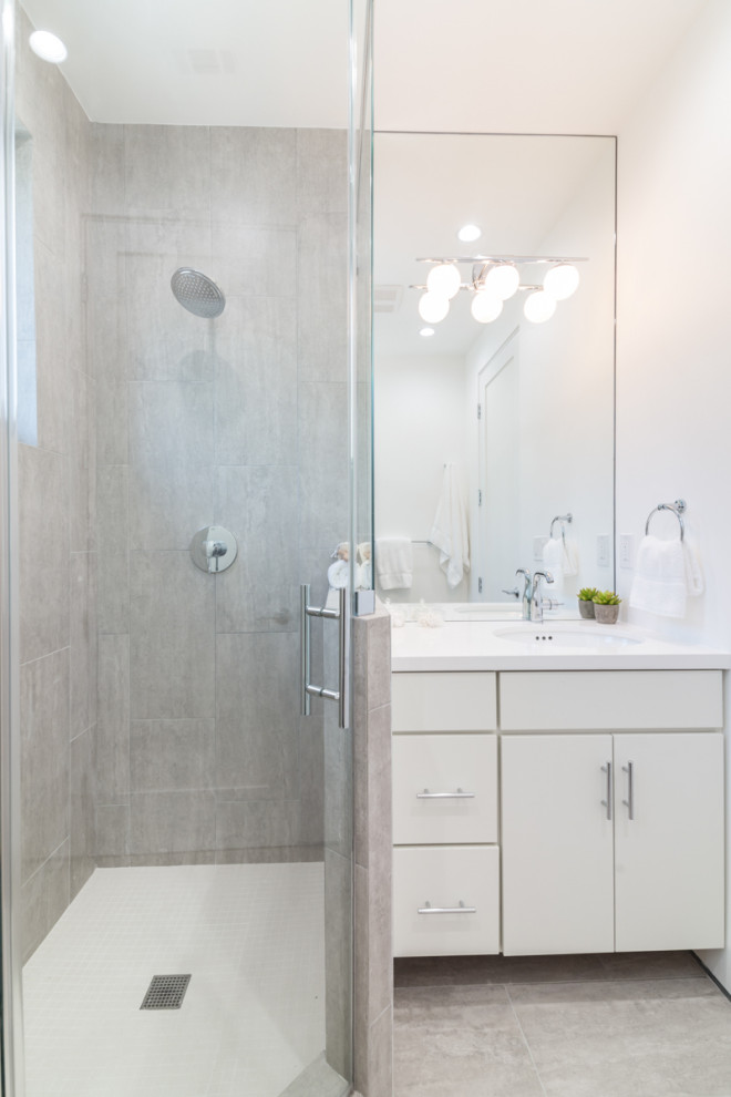 Mid-sized modern 3/4 bathroom in Los Angeles with flat-panel cabinets, white cabinets, a corner shower, a one-piece toilet, beige tile, porcelain tile, white walls, porcelain floors, an undermount sink, solid surface benchtops, grey floor, a hinged shower door and white benchtops.