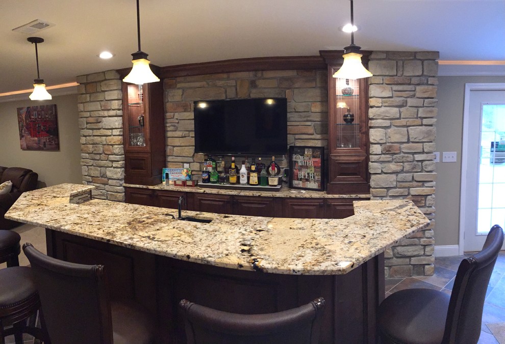 This is an example of a large arts and crafts single-wall seated home bar in St Louis with ceramic floors, an undermount sink, raised-panel cabinets, granite benchtops, beige splashback, stone tile splashback and medium wood cabinets.