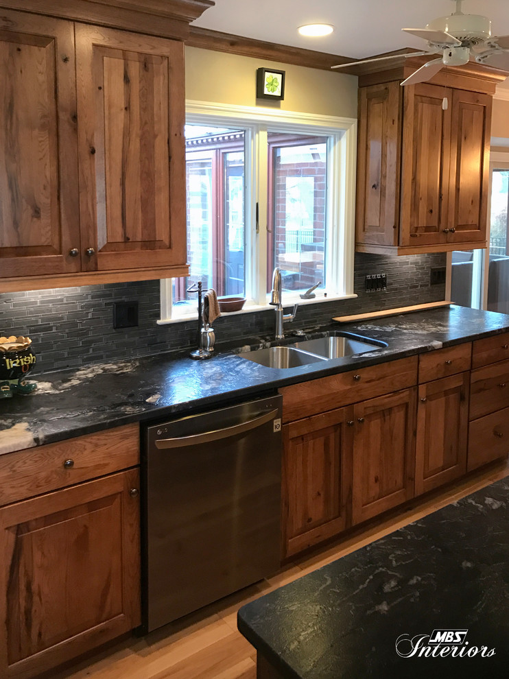 Eat-in kitchen - large rustic l-shaped light wood floor and beige floor eat-in kitchen idea with an undermount sink, raised-panel cabinets, medium tone wood cabinets, granite countertops, gray backsplash, ceramic backsplash, stainless steel appliances and an island