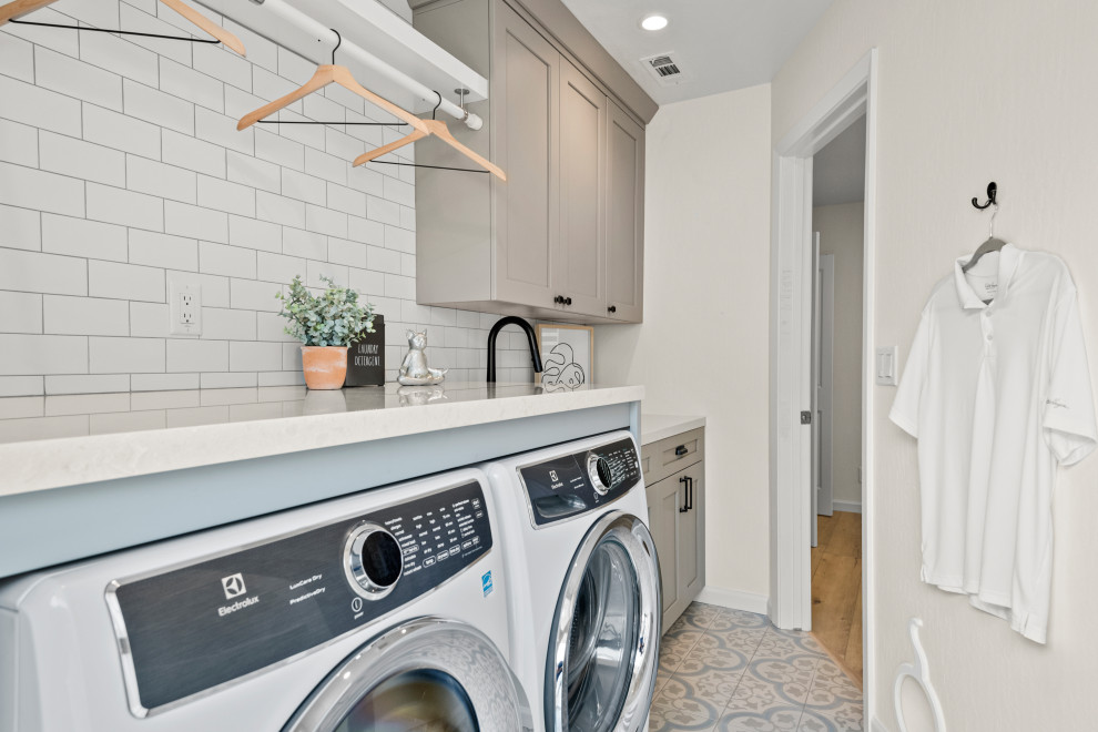 Photo of a large galley utility room in San Francisco with an undermount sink, shaker cabinets, grey cabinets, quartzite benchtops, white splashback, subway tile splashback, beige walls, ceramic floors, a side-by-side washer and dryer, multi-coloured floor and white benchtop.