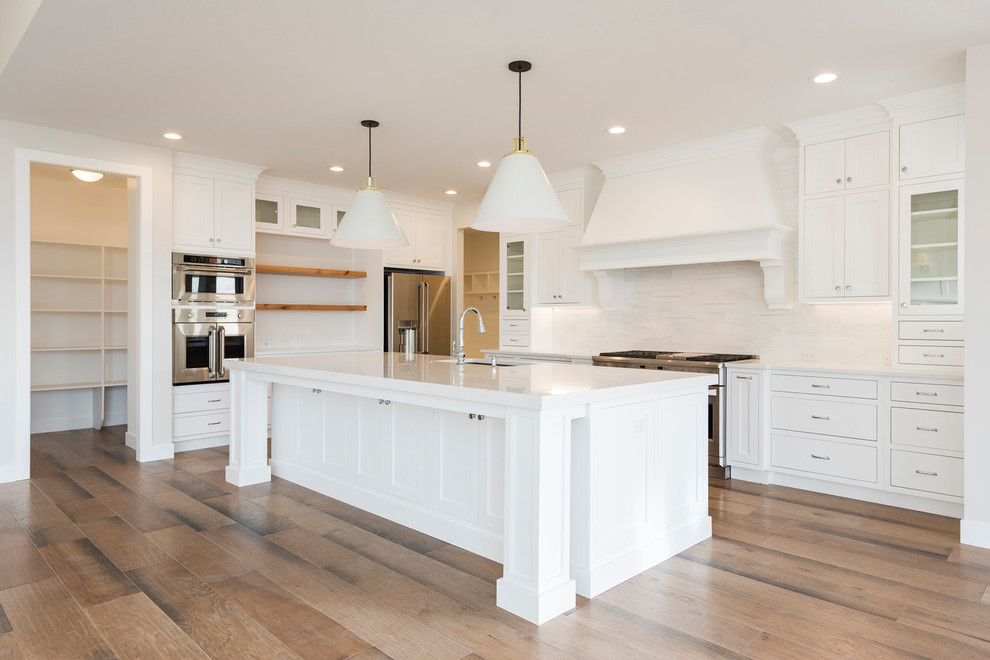 This is an example of a mid-sized contemporary l-shaped open plan kitchen in Salt Lake City with glass-front cabinets, white cabinets, granite benchtops, white splashback, ceramic splashback, stainless steel appliances, light hardwood floors, with island, brown floor and white benchtop.