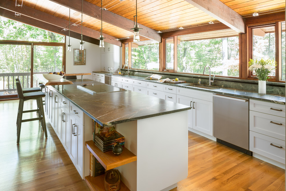 This is an example of a large midcentury galley eat-in kitchen in Boston with an undermount sink, shaker cabinets, white cabinets, soapstone benchtops, stainless steel appliances, light hardwood floors and with island.