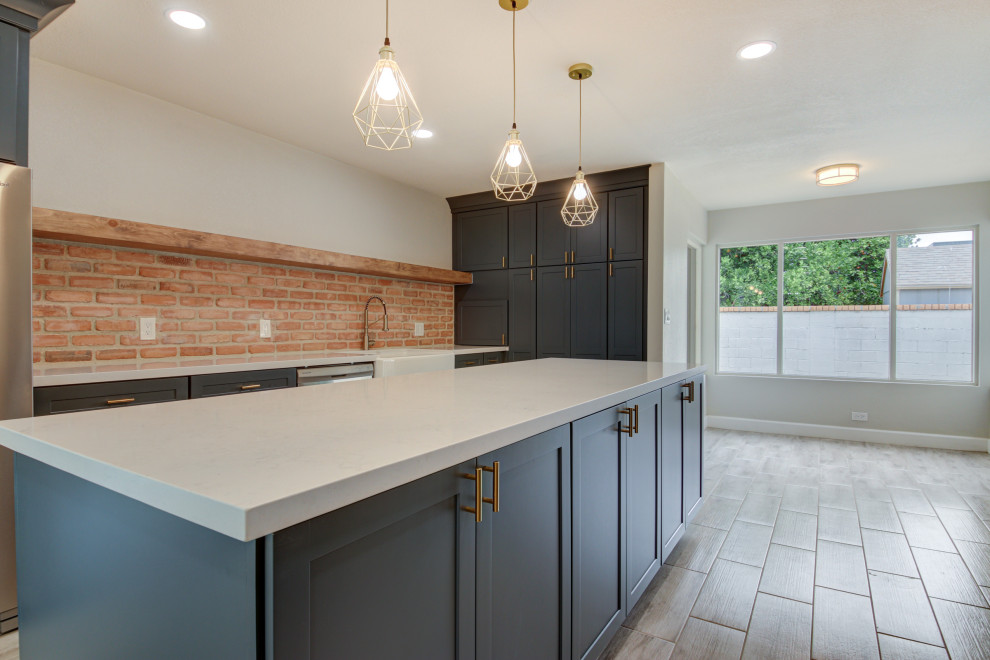 Mid-sized transitional u-shaped porcelain tile and gray floor eat-in kitchen photo in Phoenix with a farmhouse sink, shaker cabinets, blue cabinets, quartz countertops, red backsplash, brick backsplash, stainless steel appliances, an island and white countertops