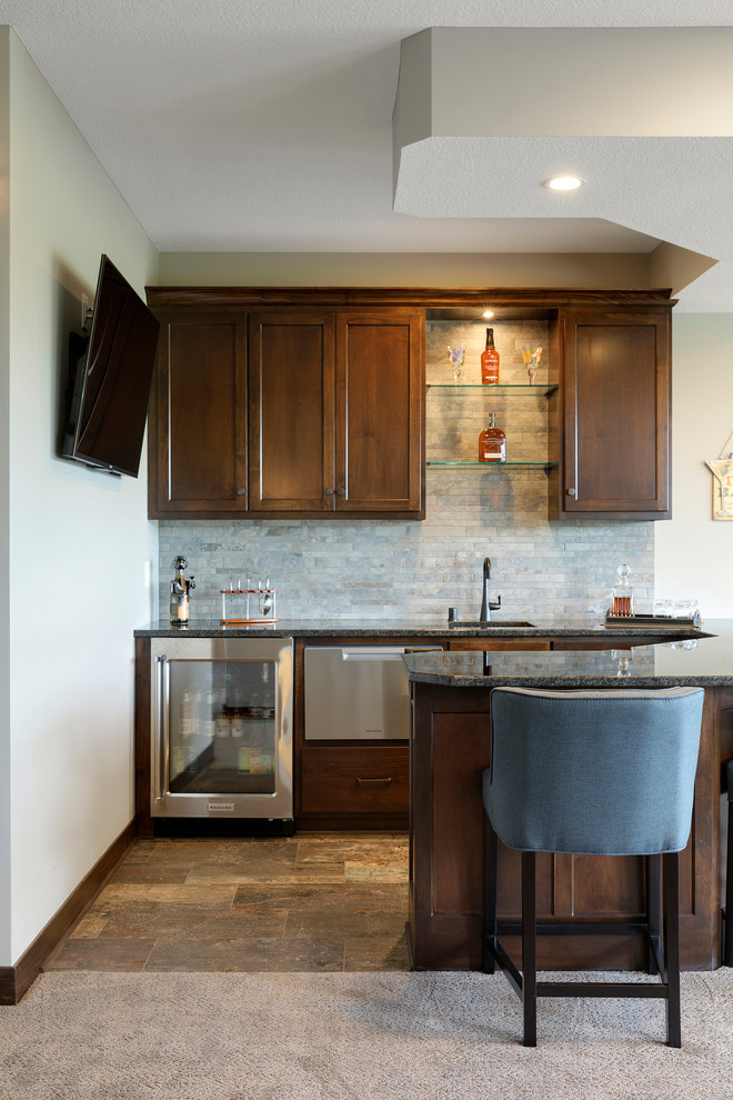 Photo of a mid-sized traditional u-shaped wet bar in Minneapolis with an undermount sink, flat-panel cabinets, medium wood cabinets, granite benchtops, beige splashback, stone tile splashback, ceramic floors, brown floor and brown benchtop.
