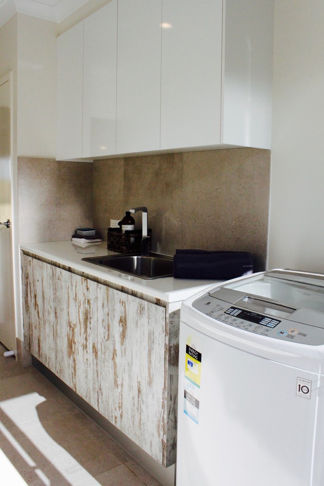 Photo of a mid-sized contemporary single-wall dedicated laundry room in Brisbane with a drop-in sink, laminate benchtops, grey walls, porcelain floors and a stacked washer and dryer.