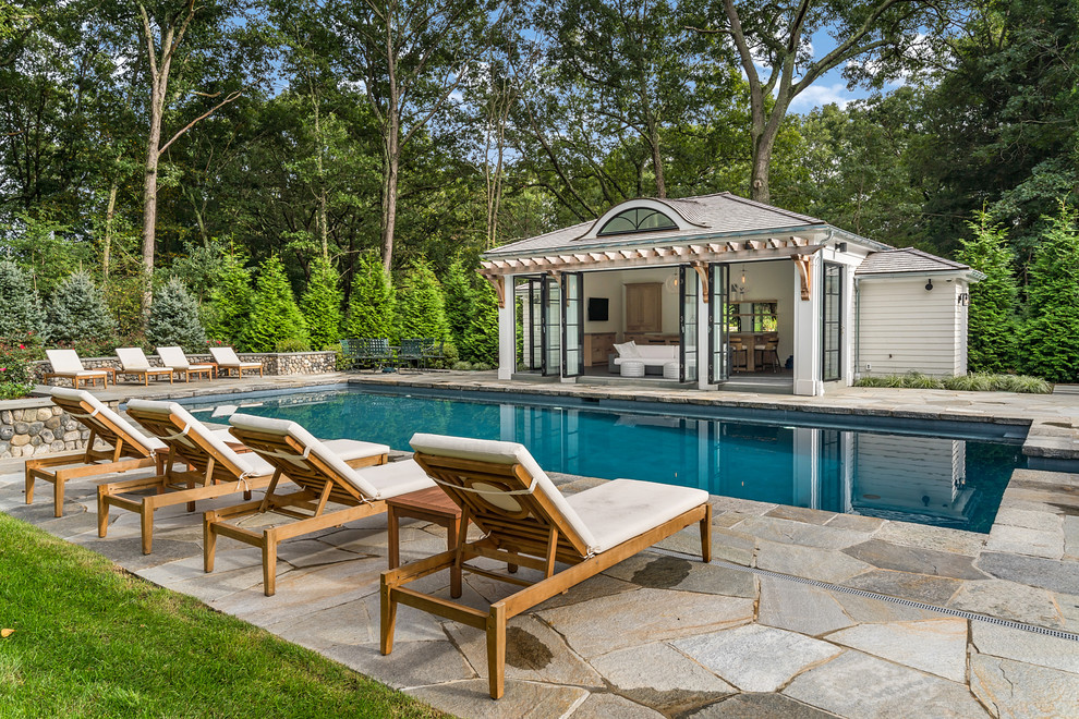This is an example of a traditional backyard rectangular lap pool in New York with a pool house and natural stone pavers.
