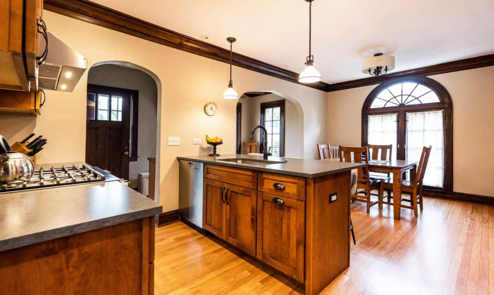 Example of a small mountain style galley medium tone wood floor and brown floor eat-in kitchen design with a drop-in sink, flat-panel cabinets, dark wood cabinets, gray backsplash, glass tile backsplash, stainless steel appliances, an island and gray countertops