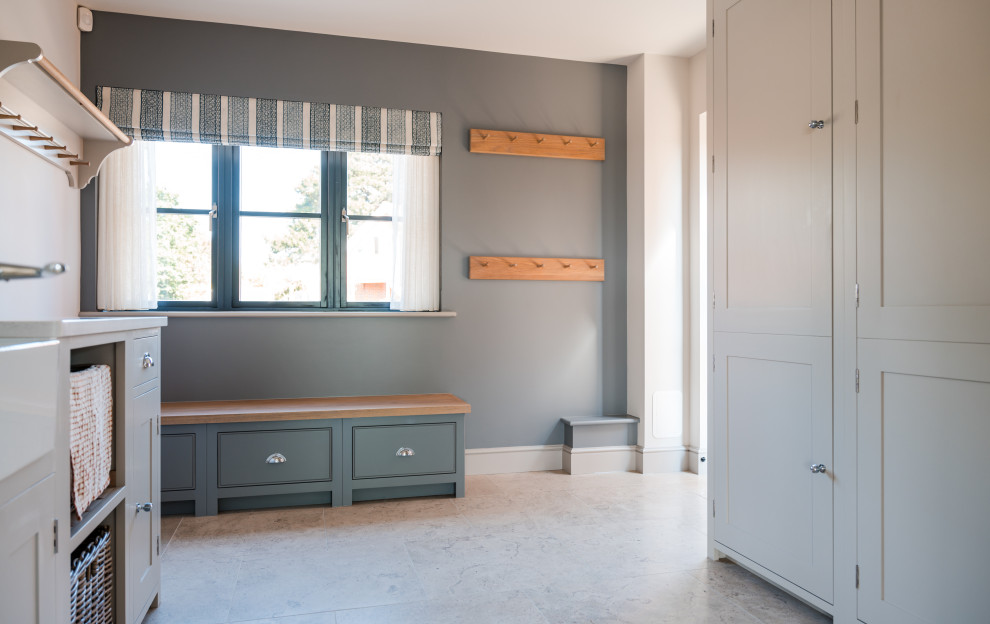 This is an example of a large beach style utility room in Hampshire with a farmhouse sink, shaker cabinets, grey cabinets, quartzite benchtops, white splashback, engineered quartz splashback, blue walls, limestone floors, an integrated washer and dryer, beige floor and white benchtop.