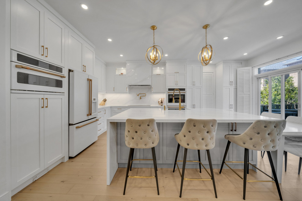 This is an example of a large contemporary l-shaped eat-in kitchen in DC Metro with a farmhouse sink, shaker cabinets, white cabinets, quartz benchtops, white splashback, engineered quartz splashback, white appliances, medium hardwood floors, with island, yellow floor and white benchtop.
