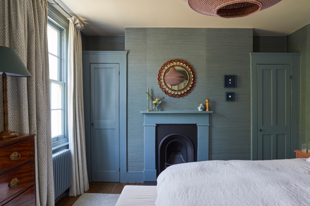 Modelo de dormitorio principal clásico renovado grande con paredes azules, suelo de madera oscura, todas las chimeneas, marco de chimenea de madera, suelo marrón y papel pintado