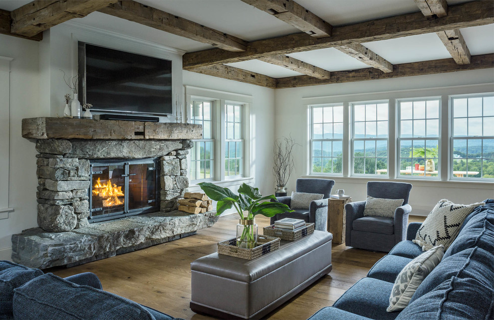 Mid-sized country formal open concept living room in Other with white walls, medium hardwood floors, a stone fireplace surround, a wall-mounted tv, brown floor and a standard fireplace.