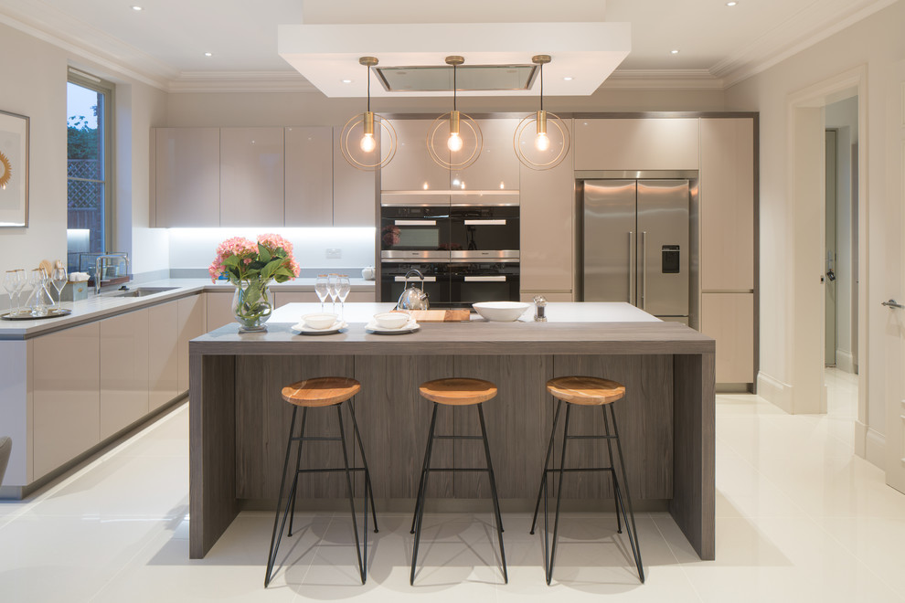 This is an example of a contemporary l-shaped kitchen in London with an undermount sink, flat-panel cabinets, beige cabinets, white splashback, stainless steel appliances, with island, beige floor and grey benchtop.
