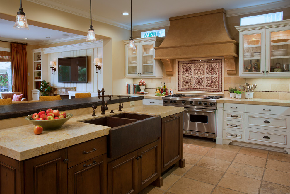 Design ideas for a large mediterranean l-shaped open plan kitchen in Orange County with a farmhouse sink, recessed-panel cabinets, white cabinets, beige splashback, stainless steel appliances, limestone splashback, limestone benchtops, limestone floors, beige floor and with island.