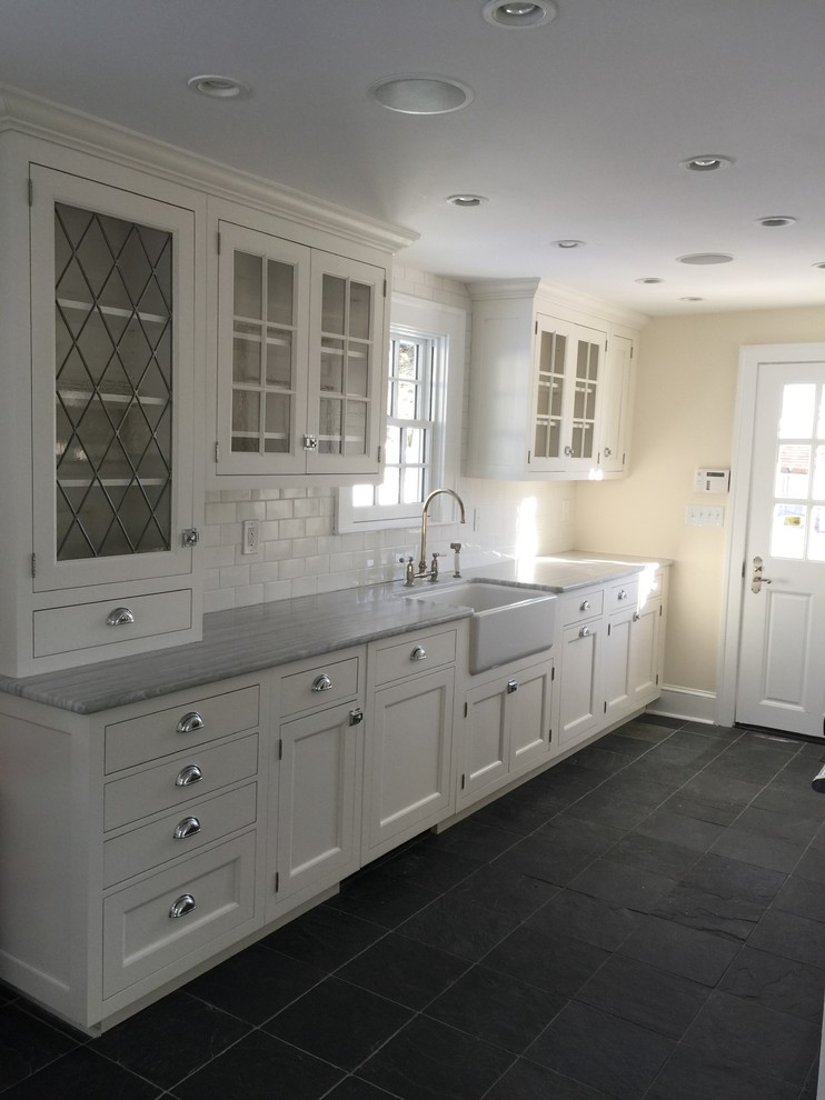 Mid-sized traditional galley open plan kitchen in New York with a farmhouse sink, shaker cabinets, white cabinets, quartzite benchtops, white splashback, subway tile splashback, stainless steel appliances, slate floors, no island and grey floor.