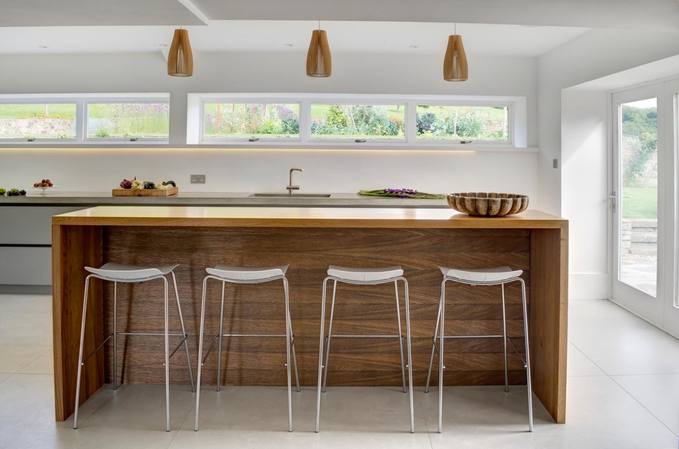This is an example of an expansive contemporary single-wall open plan kitchen in London with an integrated sink, flat-panel cabinets, white cabinets, concrete benchtops, cement tiles, a peninsula, grey floor and grey benchtop.