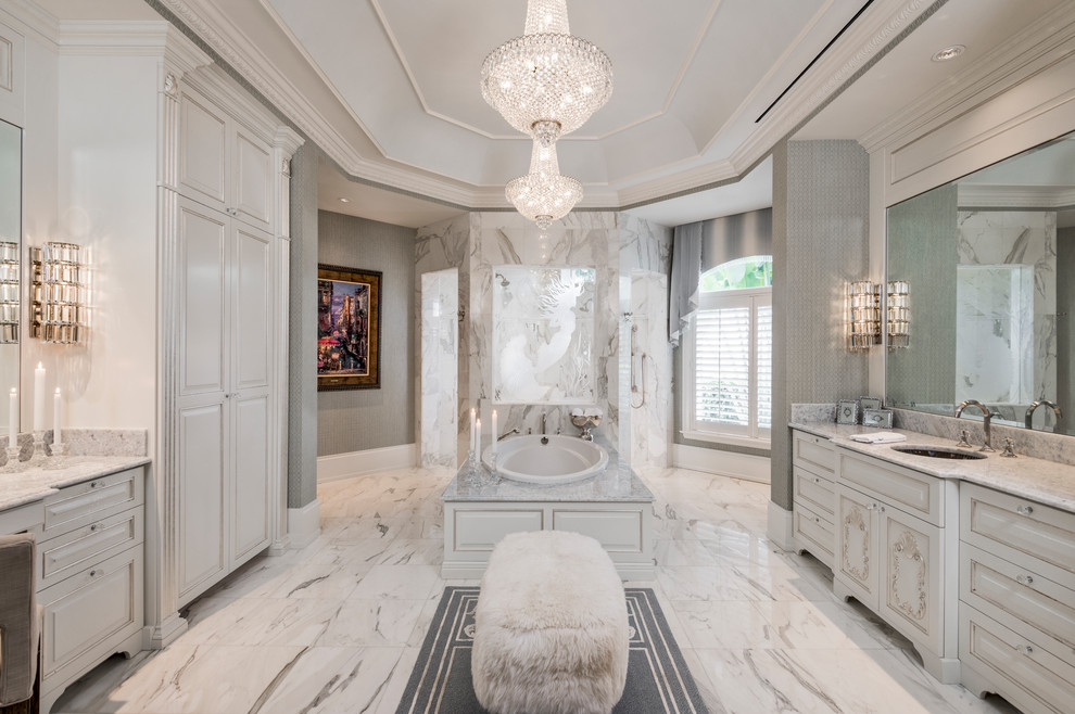 This is an example of a large traditional master bathroom in Miami with beaded inset cabinets, white cabinets, a drop-in tub, an open shower, white tile, marble, marble floors, an undermount sink, marble benchtops and grey walls.