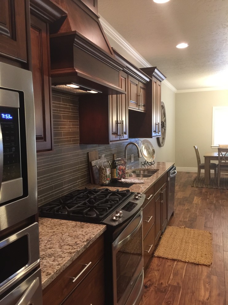 Example of a mid-sized mountain style l-shaped dark wood floor open concept kitchen design in Boise with an undermount sink, raised-panel cabinets, dark wood cabinets, granite countertops, gray backsplash, glass tile backsplash, stainless steel appliances and an island