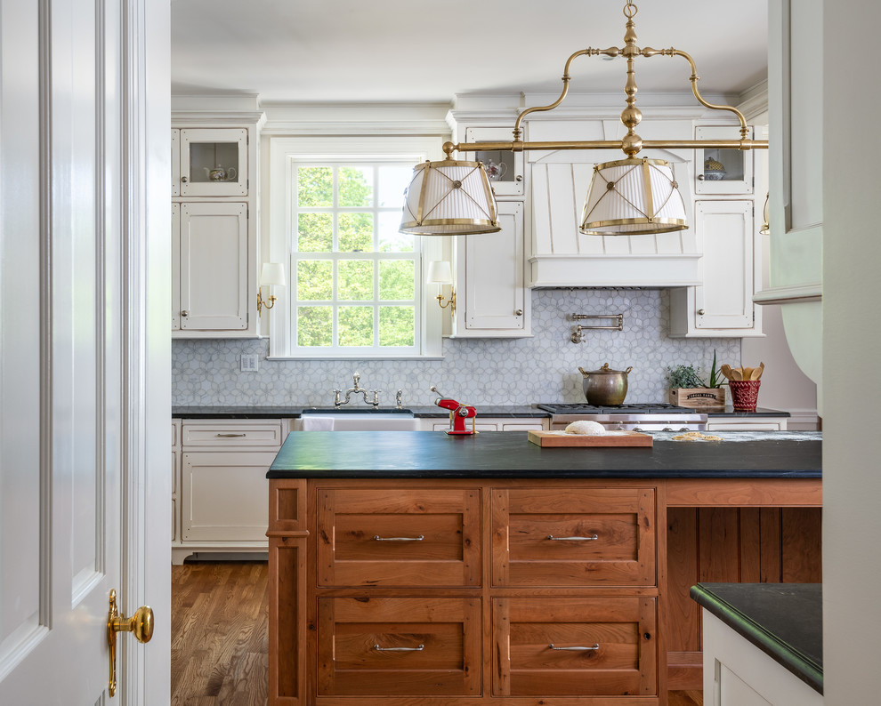 Inspiration for a large transitional u-shaped separate kitchen in DC Metro with a farmhouse sink, recessed-panel cabinets, white cabinets, soapstone benchtops, white splashback, panelled appliances, medium hardwood floors, with island, brown floor and black benchtop.