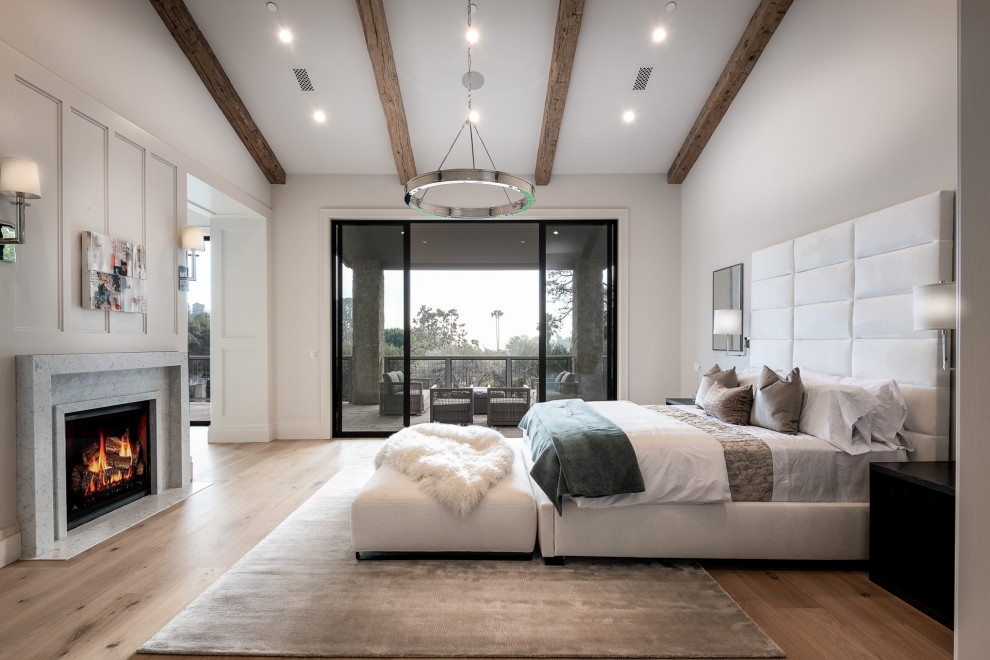 Example of a large farmhouse master light wood floor, beige floor, exposed beam and wall paneling bedroom design in Los Angeles with white walls, a two-sided fireplace and a stacked stone fireplace