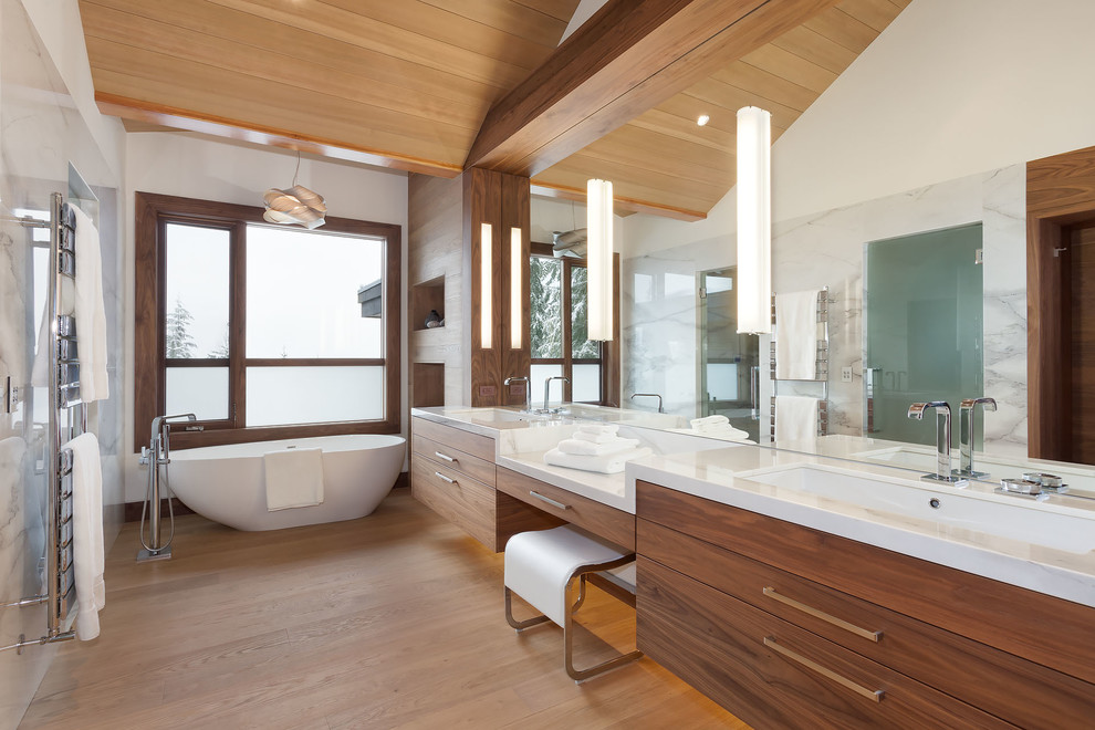 Contemporary master bathroom in Vancouver with flat-panel cabinets, medium wood cabinets, a freestanding tub, marble, white walls, light hardwood floors, an undermount sink, beige floor, a hinged shower door and white tile.