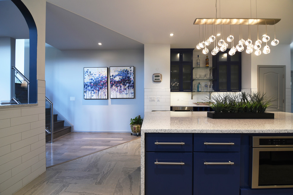 Design ideas for a large contemporary l-shaped wet bar in Baltimore with quartz benchtops, white splashback, ceramic splashback, porcelain floors, no sink, glass-front cabinets and blue cabinets.
