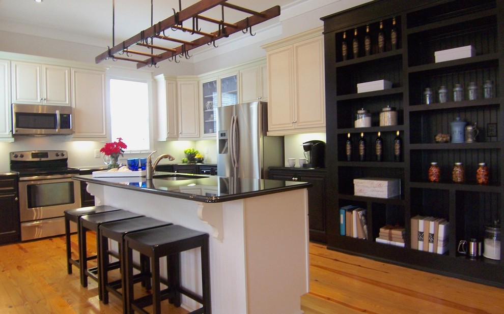 This is an example of a mid-sized traditional l-shaped eat-in kitchen in Raleigh with light hardwood floors, with island, an undermount sink, raised-panel cabinets, white cabinets, stainless steel appliances and brown floor.