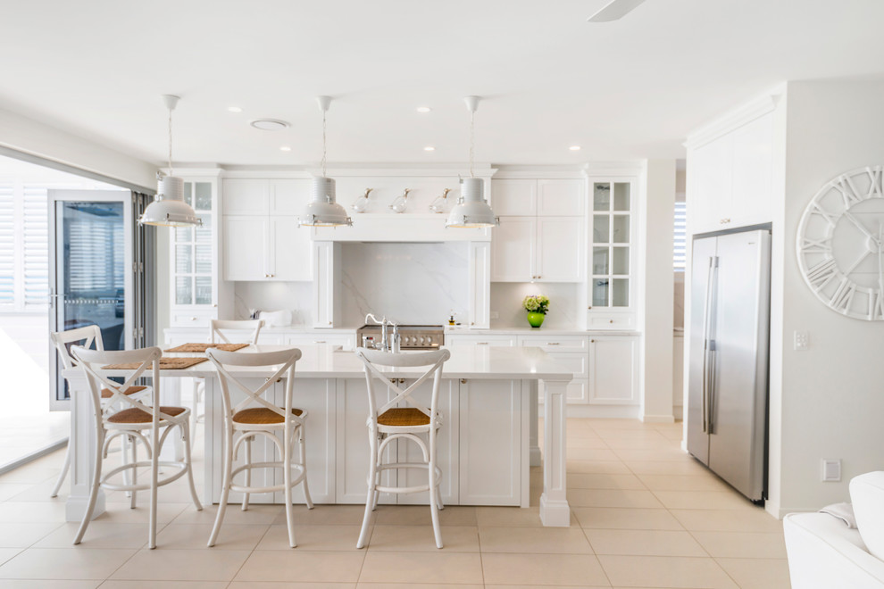 Design ideas for a large beach style galley eat-in kitchen in Gold Coast - Tweed with a farmhouse sink, shaker cabinets, white cabinets, marble benchtops, white splashback, marble splashback, stainless steel appliances, ceramic floors, with island, beige floor and white benchtop.