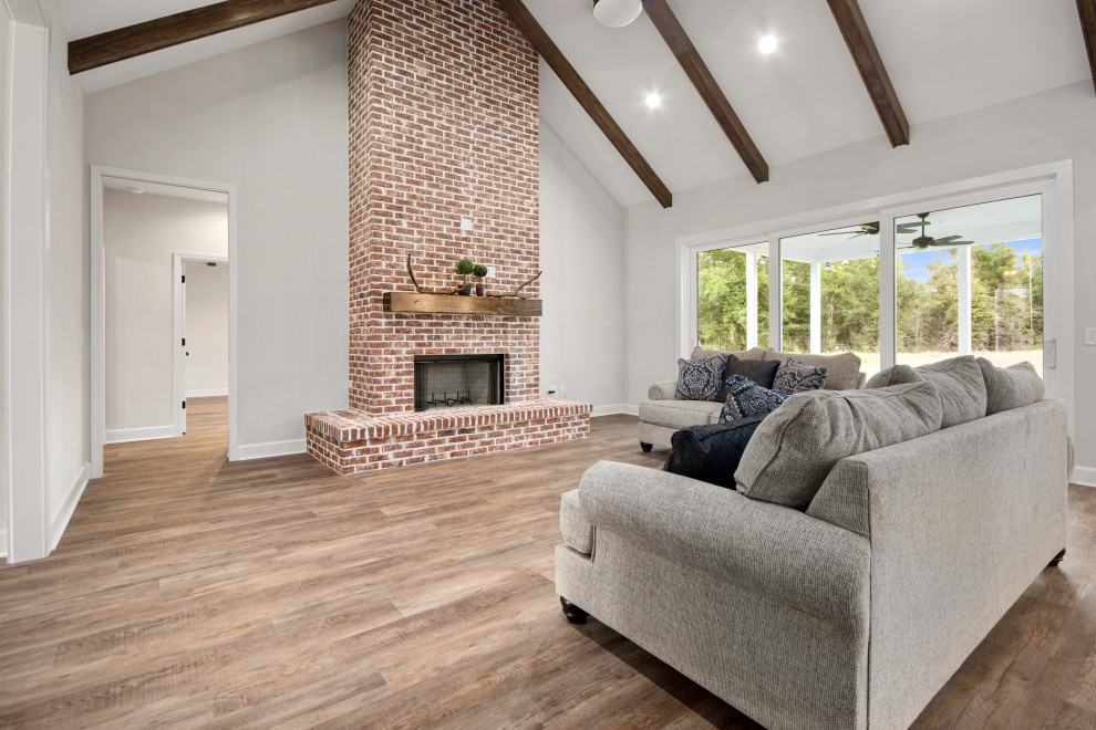 Photo of a medium sized farmhouse open plan games room in Other with grey walls, vinyl flooring, a standard fireplace, a brick fireplace surround, a wall mounted tv, brown floors and a vaulted ceiling.