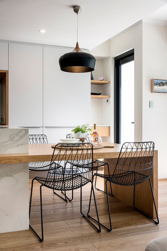 Design ideas for a large scandinavian galley open plan kitchen in Perth with a single-bowl sink, flat-panel cabinets, white cabinets, quartz benchtops, metallic splashback, mirror splashback, black appliances, light hardwood floors, with island, brown floor and white benchtop.
