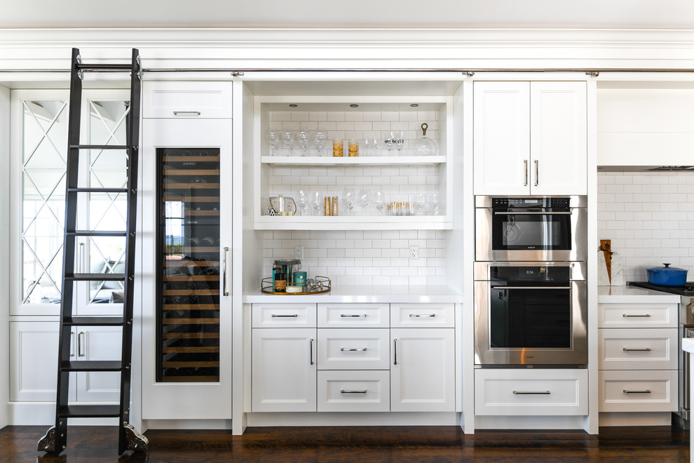 Transitional dark wood floor and brown floor kitchen photo in Toronto with shaker cabinets, white cabinets, white backsplash, subway tile backsplash, stainless steel appliances and white countertops