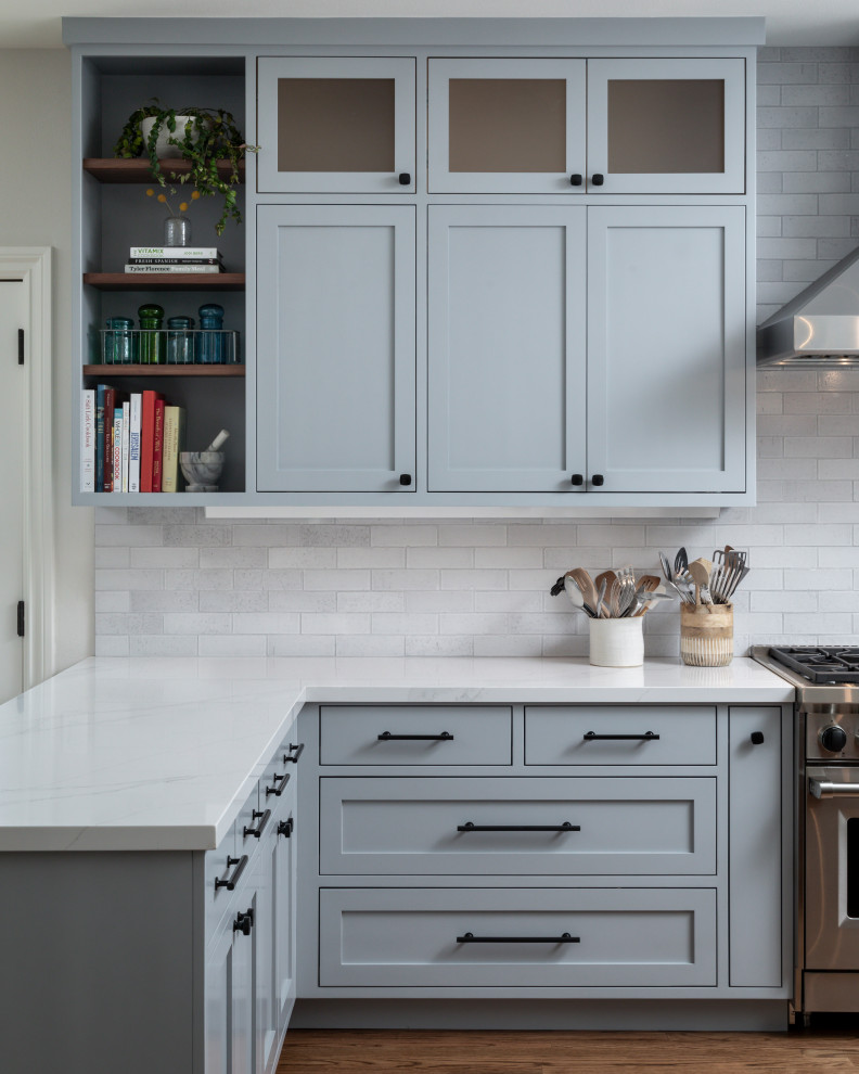 Example of a large transitional u-shaped medium tone wood floor and brown floor eat-in kitchen design in San Francisco with a farmhouse sink, shaker cabinets, medium tone wood cabinets, quartz countertops, white backsplash, brick backsplash, stainless steel appliances, two islands and white countertops