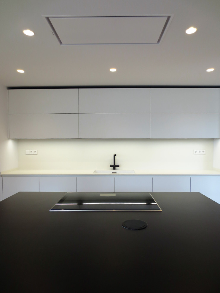 Mid-sized contemporary single-wall eat-in kitchen in Barcelona with an undermount sink, recessed-panel cabinets, white cabinets, quartz benchtops, white splashback, black appliances, with island and black benchtop.