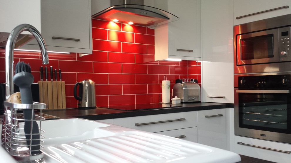 Bild på ett avskilt, litet funkis u-kök, med en nedsänkt diskho, släta luckor, vita skåp, laminatbänkskiva, rött stänkskydd, stänkskydd i keramik, rostfria vitvaror och skiffergolv