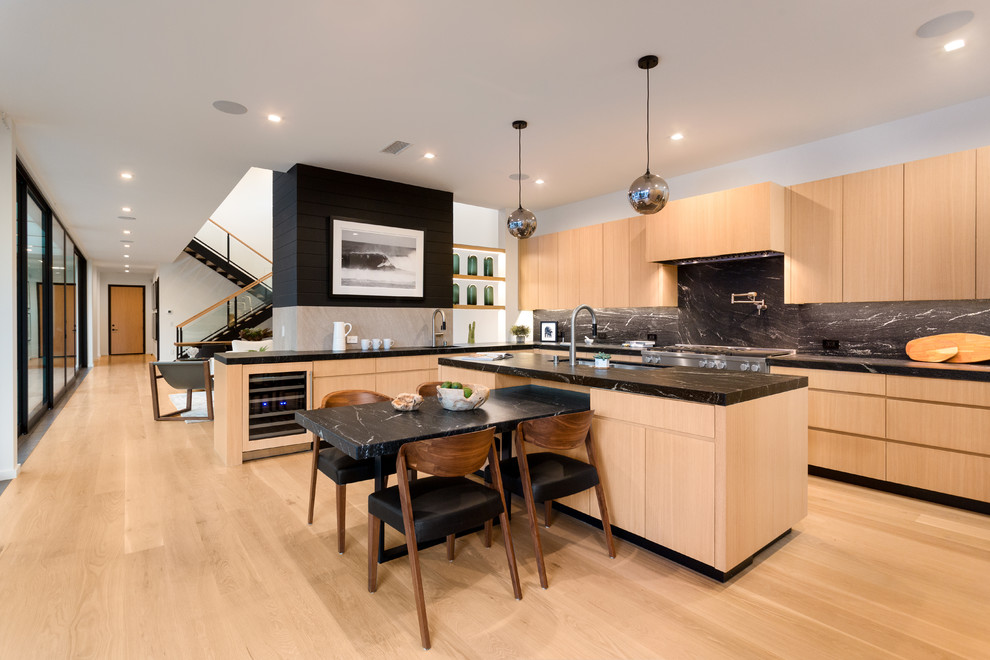 Large contemporary u-shaped open plan kitchen in Los Angeles with an undermount sink, flat-panel cabinets, light wood cabinets, marble benchtops, black splashback, stone slab splashback, stainless steel appliances, light hardwood floors, with island, beige floor and black benchtop.