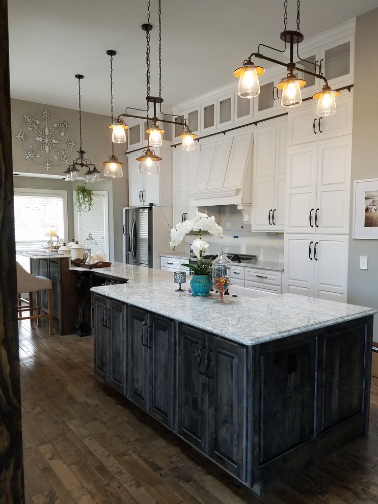 Photo of a large traditional single-wall eat-in kitchen in St Louis with a farmhouse sink, raised-panel cabinets, white cabinets, quartz benchtops, white splashback, glass tile splashback, stainless steel appliances, dark hardwood floors, with island and black floor.