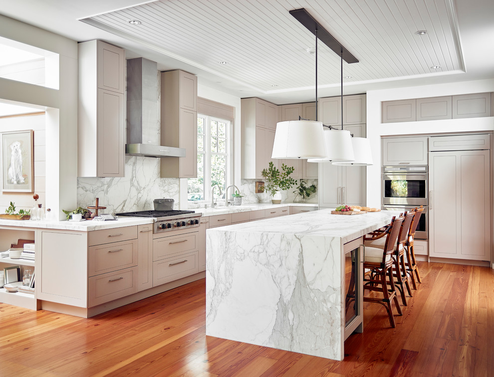 Photo of a large traditional l-shaped kitchen in Denver with recessed-panel cabinets, marble benchtops, white splashback, marble splashback, stainless steel appliances, medium hardwood floors, with island, beige cabinets and orange floor.