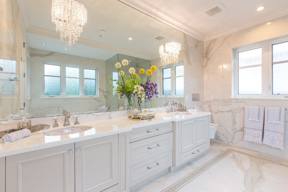 Photo of a traditional bathroom in Vancouver with recessed-panel cabinets, white cabinets, a corner shower, a wall-mount toilet, white walls, marble floors, an undermount sink and white tile.