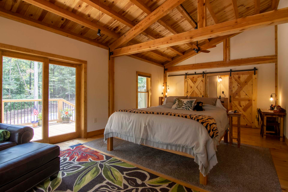 Large mountain style master light wood floor, brown floor and vaulted ceiling bedroom photo with beige walls