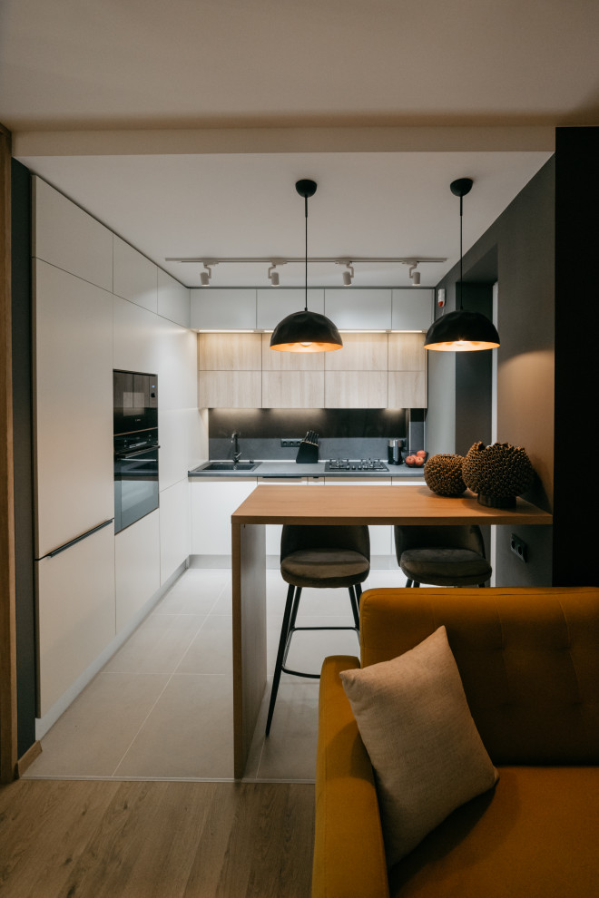Mid-sized contemporary l-shaped open plan kitchen in Other with an undermount sink, flat-panel cabinets, white cabinets, laminate benchtops, black splashback, black appliances, porcelain floors, a peninsula, grey floor and black benchtop.