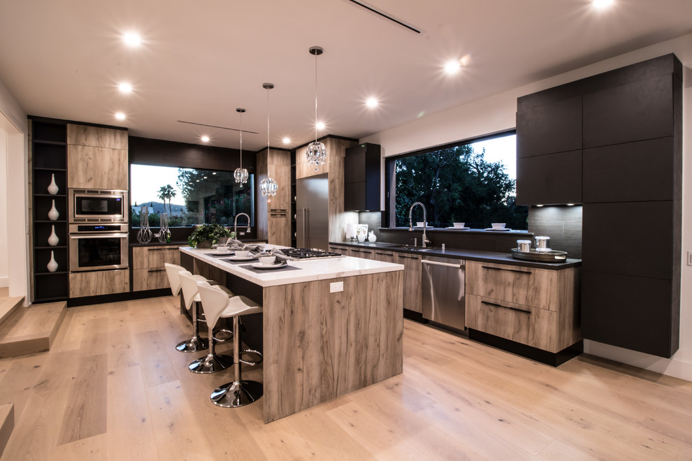 This is an example of a large modern l-shaped eat-in kitchen in Los Angeles with an undermount sink, flat-panel cabinets, brown cabinets, quartzite benchtops, black splashback, porcelain splashback, stainless steel appliances, light hardwood floors, with island, brown floor and grey benchtop.