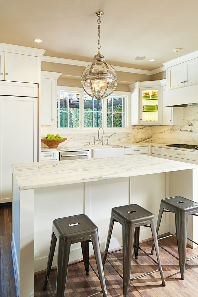 This is an example of a traditional l-shaped separate kitchen in Dallas with a farmhouse sink, white cabinets, white splashback, stone slab splashback, with island, marble benchtops, stainless steel appliances and medium hardwood floors.