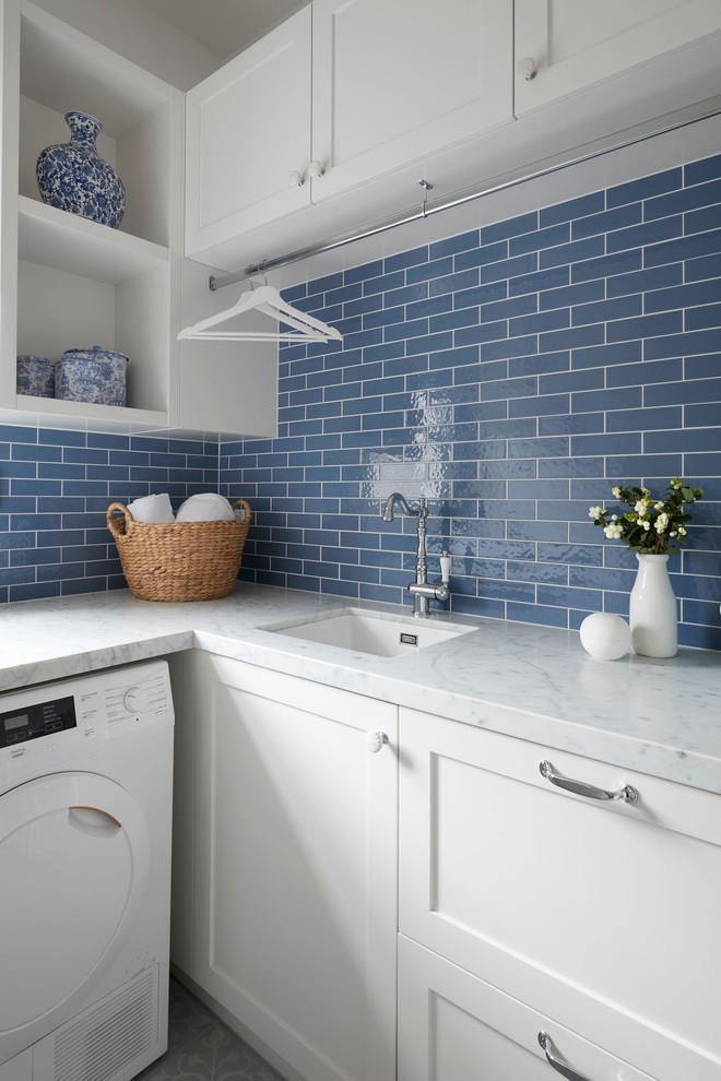 Photo of a small transitional l-shaped utility room in Melbourne with a drop-in sink, beaded inset cabinets, white cabinets, marble benchtops, blue walls, ceramic floors, an integrated washer and dryer, multi-coloured floor and white benchtop.