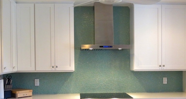 This is an example of a mid-sized beach style u-shaped kitchen in Tampa with an undermount sink, shaker cabinets, white cabinets, solid surface benchtops, blue splashback, glass tile splashback and panelled appliances.