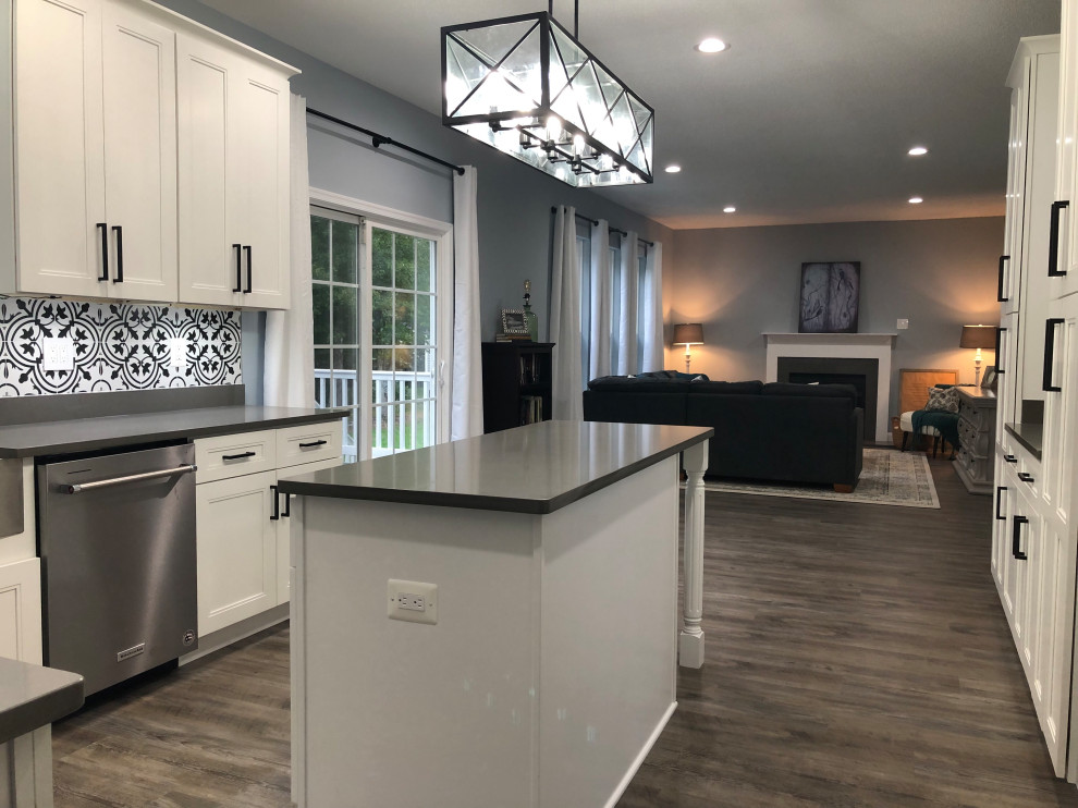 Mid-sized farmhouse l-shaped vinyl floor and gray floor eat-in kitchen photo in DC Metro with a farmhouse sink, shaker cabinets, white cabinets, quartz countertops, black backsplash, porcelain backsplash, stainless steel appliances, an island and gray countertops