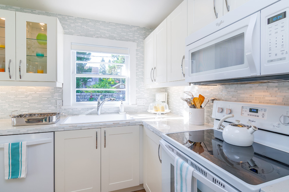Photo of a small traditional l-shaped kitchen in Tampa with a single-bowl sink, shaker cabinets, white cabinets, tile benchtops, multi-coloured splashback, glass sheet splashback, white appliances and light hardwood floors.